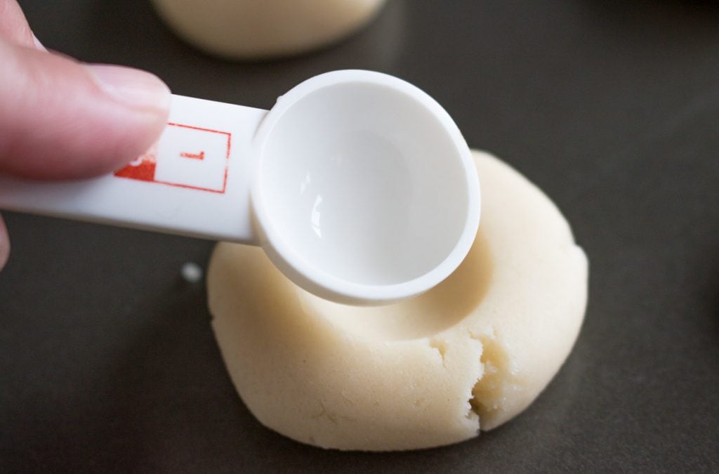  using measuring spoon to create indent in top of thumbprint cookies with icing