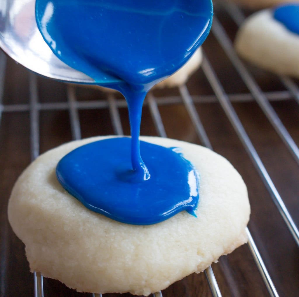 pouring blue icing on top of thumbprint cookies to make thumbprint cookies with icing