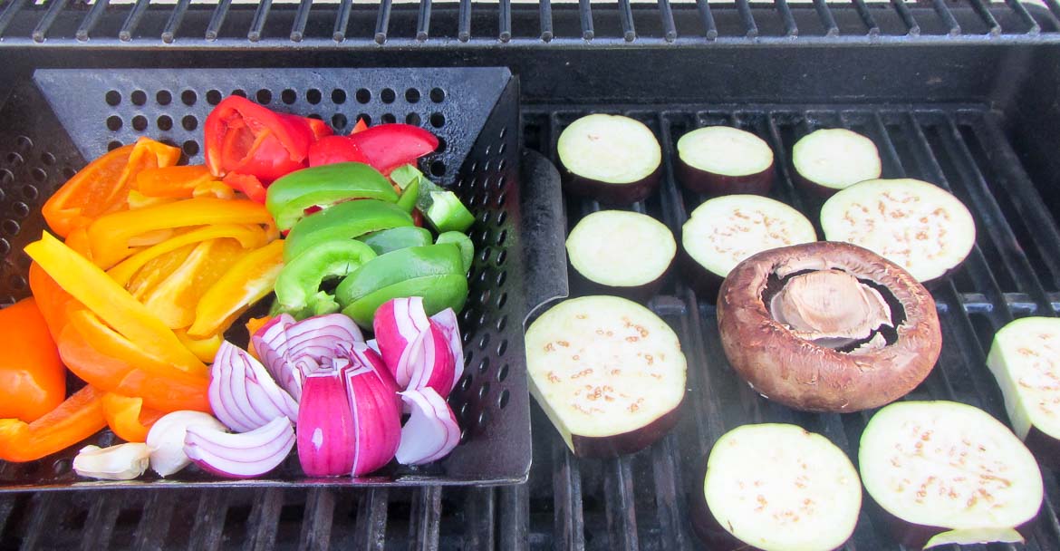 veggies grilling in a basket with portabella mushroom and eggplant slices on the side