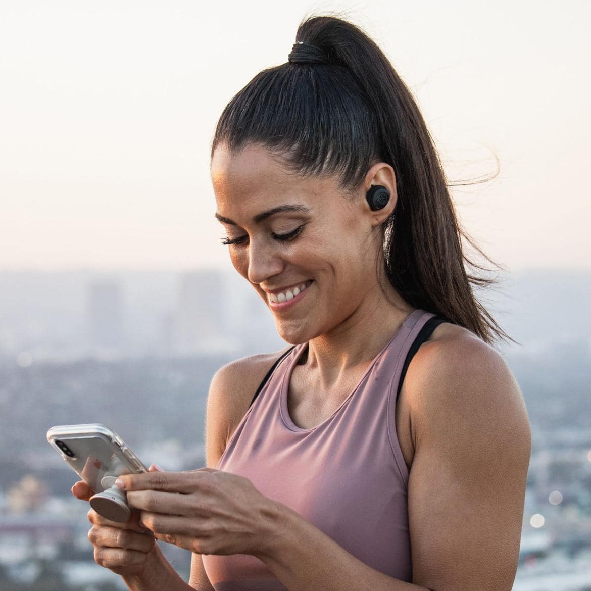 JLab true wireless earbuds under $100 worn by woman holding smartphone