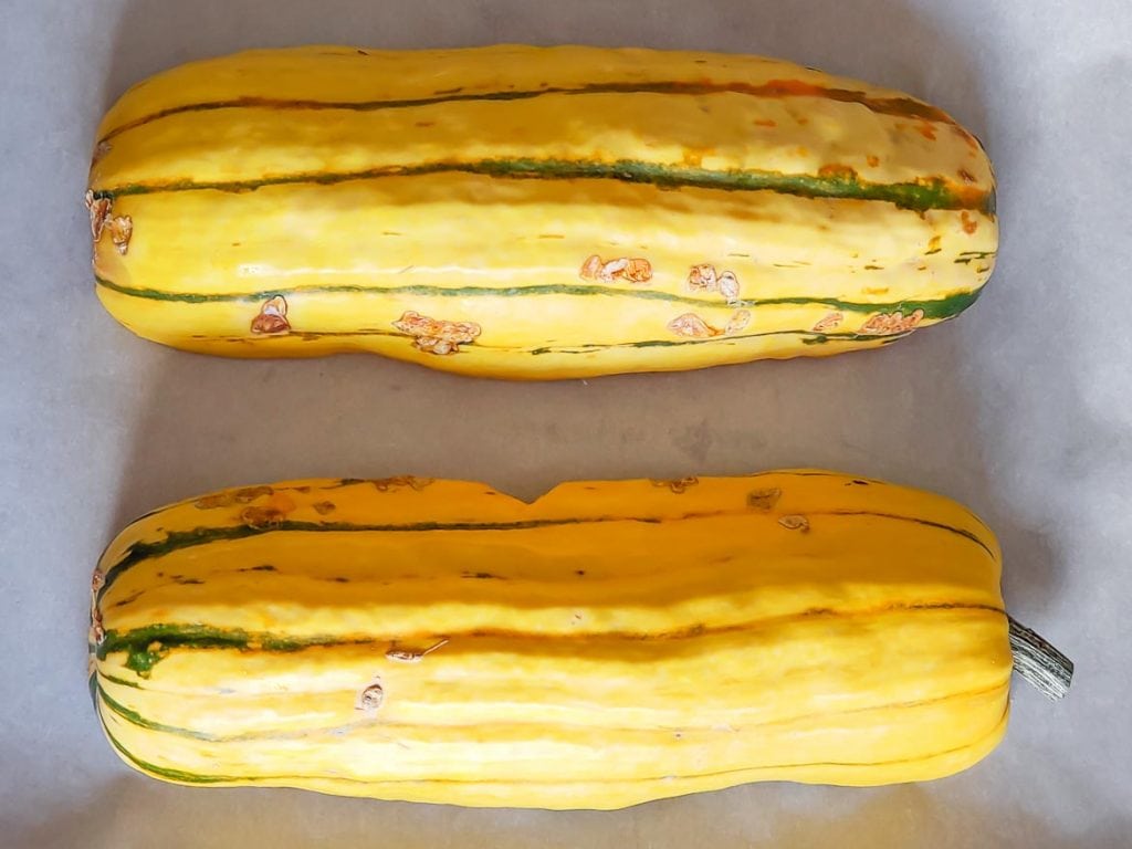 delicata squash halves ready for baking on parchment paper