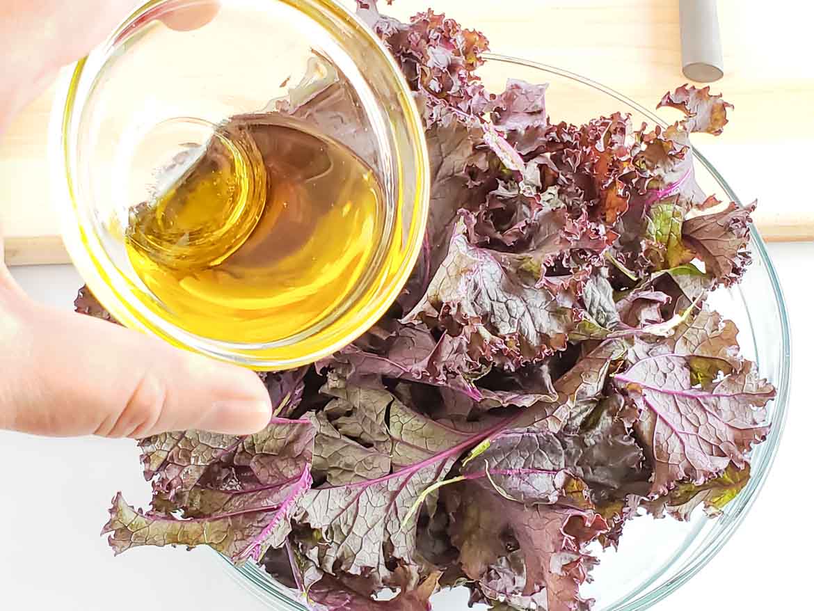 adding olive oil to purple kale chips