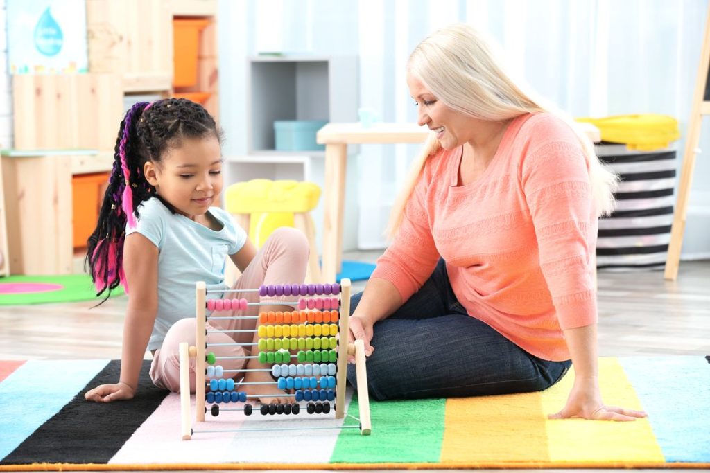 Things to know before hiring a nanny - nanny playing with young girl on play mat DP