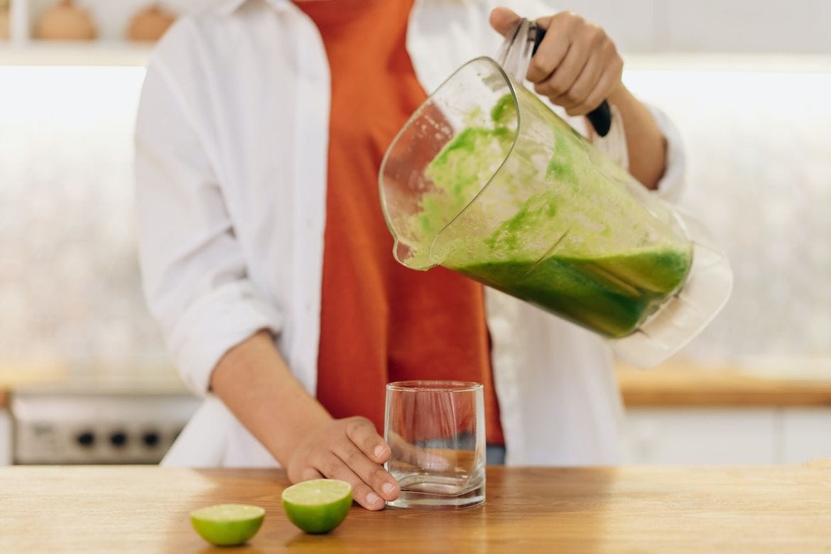 pouring a smoothie from a blender jar to a glass with a  juicer blender combo