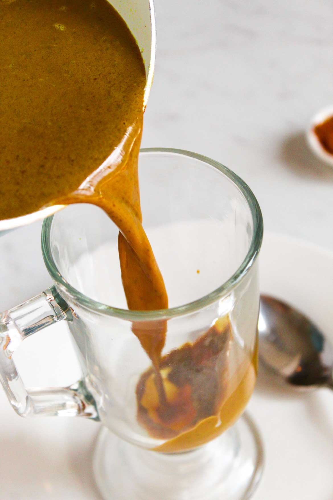 turmeric hot cocoa poured from saucepan into glass mug