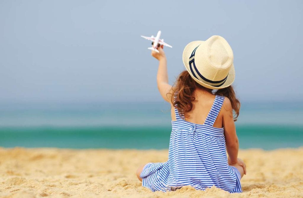 Young girl at the beach holding up an airplane toy