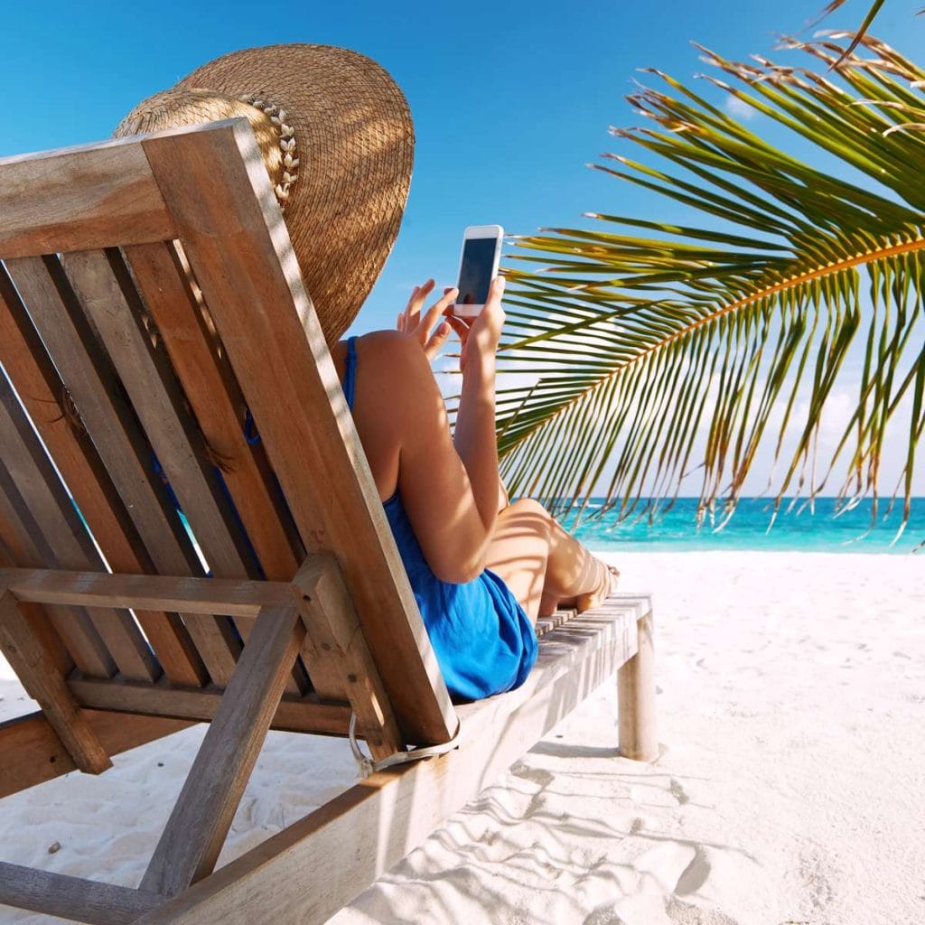 woman on a beach chair with phone for article How to Prepare Your Phone for a Family Vacation