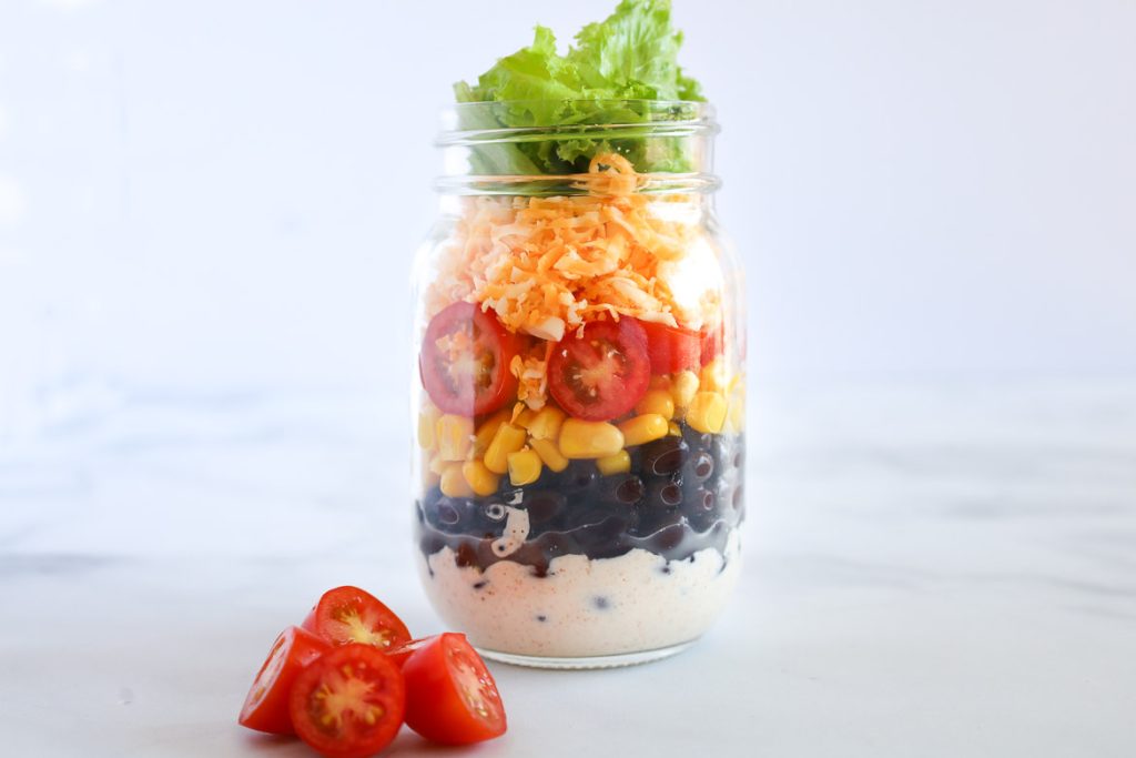 mason jar Mexican salad made with sour cream black beans tomatoes cheddar corn and lettuce