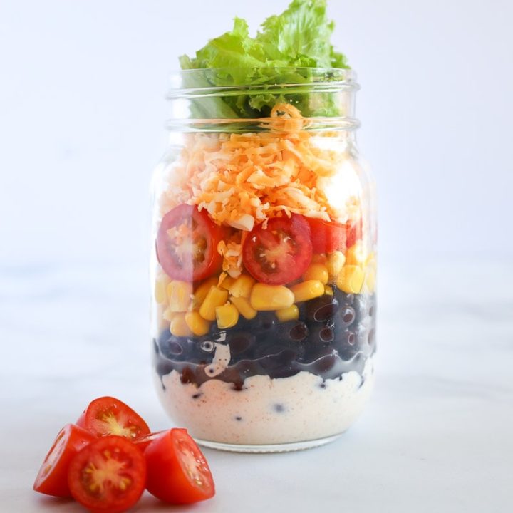 mason jar Mexican salad made with sour cream black beans tomatoes cheddar corn and lettuce
