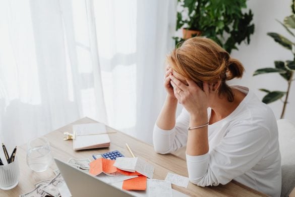woman with head in hands at desk with laptop and coffee for article How Technology Is Making Financial Planning More Accessible