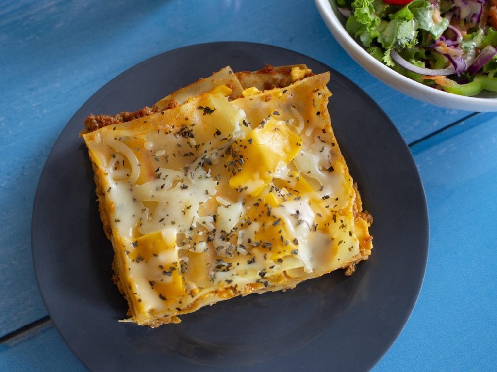 lasagna with white sauce on a dark plate and salad