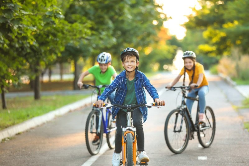 Smiling kids on bikes riding down a tree lined neighborhood