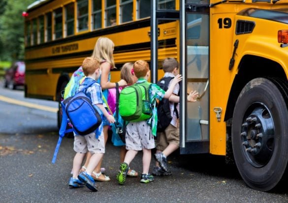 Kids in colorful backpacks getting on a yellow school bus
