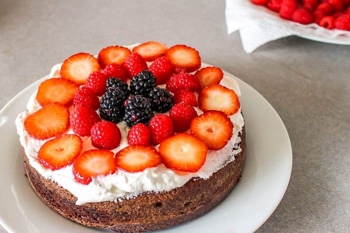 bottom half done of two layer cake with whipped cream on chocolate black forest cake with fresh strawberries, raspberries and blackberries