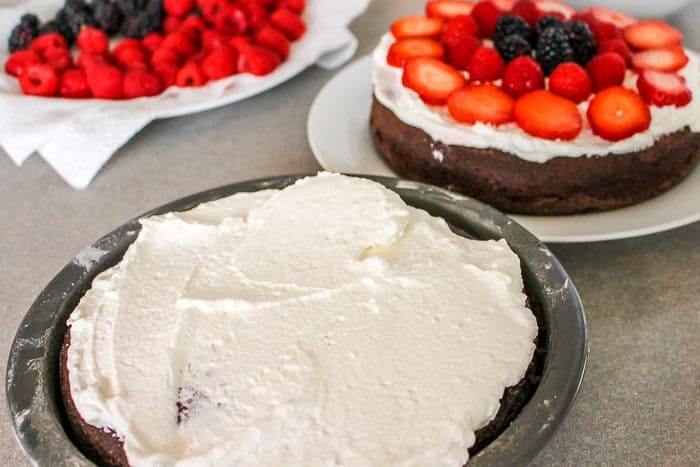 half of cake frosted with whipped cream on chocolate black forest cake with fresh strawberries, raspberries and blackberries