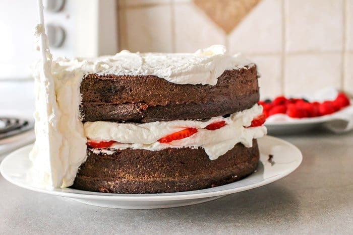 half iced cake with whipped cream frosting on chocolate cake with fresh berries